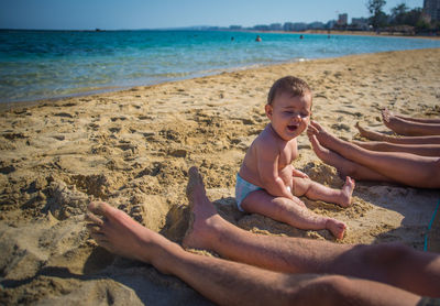 Low section of family by baby boy yawning at beach