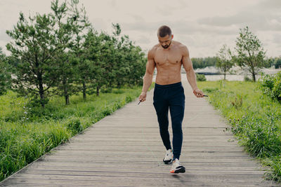 Full length of shirtless man skipping on footpath