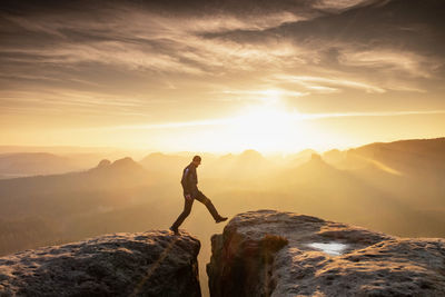 Strong mountain climber hiking and jumping over ridge of a peaks at sunset. man takes leap of faith