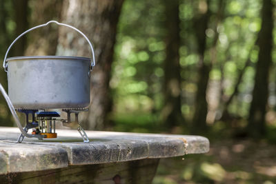 A titanium pot for making food on a gas stove on a camping wooden table in the forest.