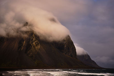 Scenic view of sea by mountain against sky