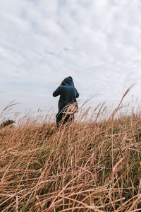 Rear view of man standing on grassy field against cloudy sky