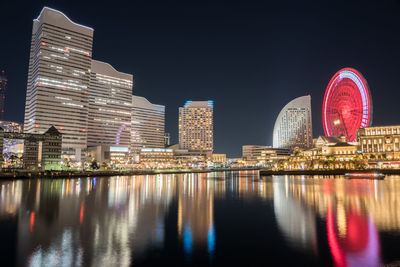 Illuminated buildings by river against sky in city at night