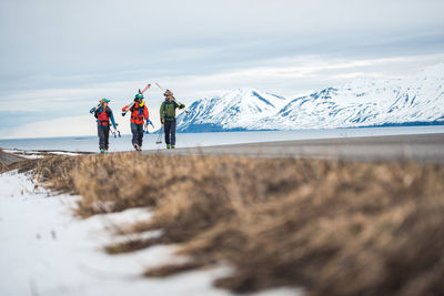 Three people walk along a paved road with mountains and ocean behind