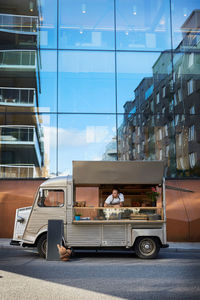 Young male owner in food truck parked on city street against glass building