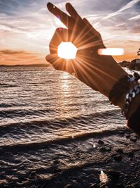 Man hand by sea against sky during sunset