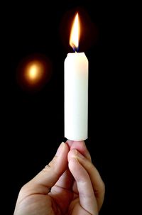 Close-up of hand holding candle against black background