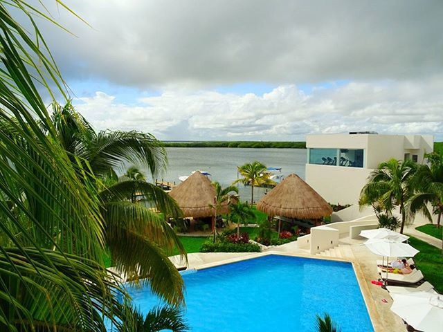 palm tree, sky, water, cloud - sky, sea, building exterior, built structure, architecture, cloudy, tree, cloud, house, horizon over water, tourist resort, nature, tranquility, swimming pool, beauty in nature, scenics, tranquil scene