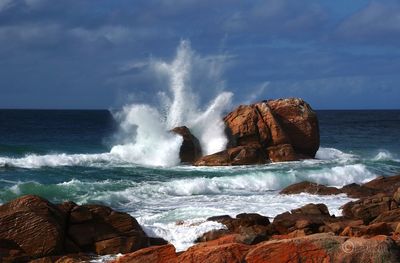 Waves breaking on rocks at shore against sky