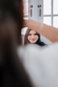 Portrait of young woman standing against window