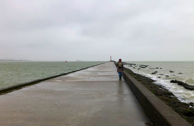 Rear view of man walking on beach against sky