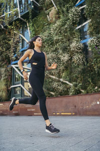 Side view of young female jogger running in a city with a garden facade building in the background