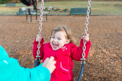 Cropped hand reaching towards happy daughter playing on swing