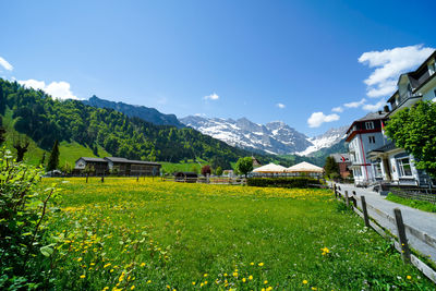 Scenic view of field by houses and mountains against sky