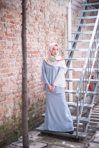 Full length of smiling young woman standing against brick wall