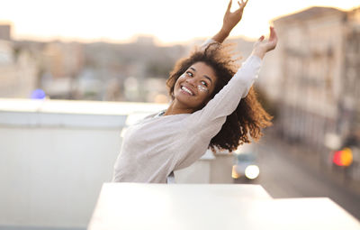 Portrait of smiling young woman with arms raised standing in cafe