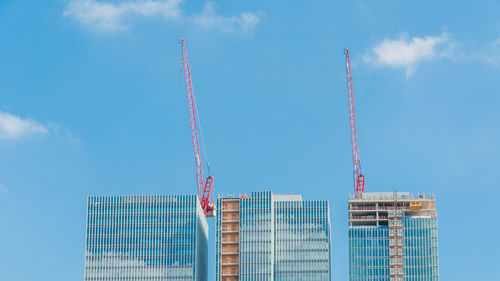 Low angle view of crane by building against sky