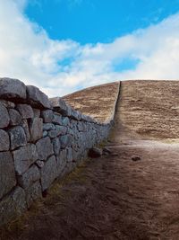 Footpath leading towards wall against sky