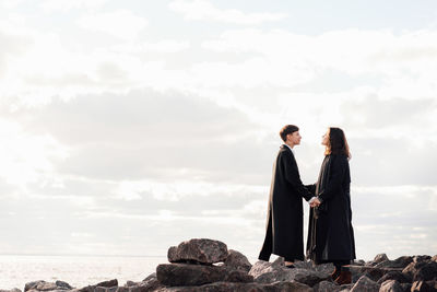 Portrait of lesbian women holding hands while standing on rock against sea and sky