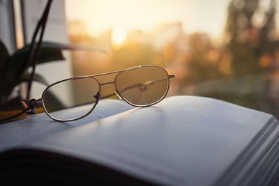 Reading glasses and an open book on the windowsill against the backdrop of the sun. 