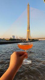 A hand is holding a glass of cocktail with beautiful view of bangkok and chaophraya river. 