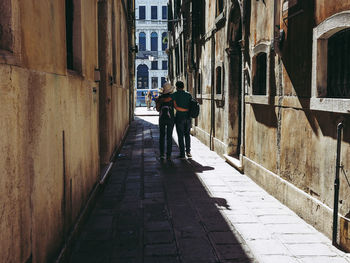 Rear view of men walking on footpath amidst buildings in city