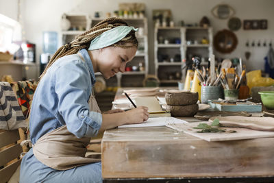 Smiling craftsperson drawing on sketch pad at art studio