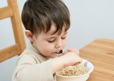 Little boy eating oatmeal for breakfast in the kitchen