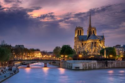 Notre dame de paris by seine river against cloudy sky during sunset