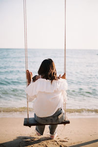 Rear view of boy swinging at beach