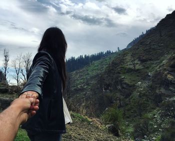 Cropped image of man holding girlfriend hand while walking towards mountains