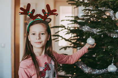 Portrait of a girl next to the new year tree, holding a christmas tree decoration in her hands 