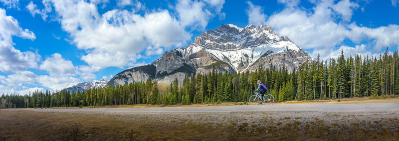 Side view of woman mountain biking by trees and mountain at banff national park