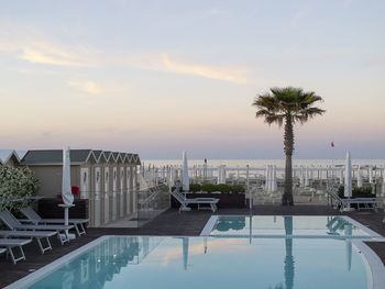 Palm trees by swimming pool against sky during sunset