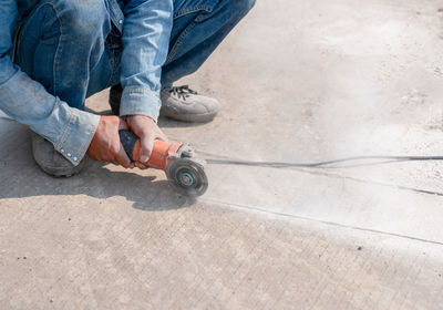 Worker cutting concrete floor with electric hand saw at construction site.