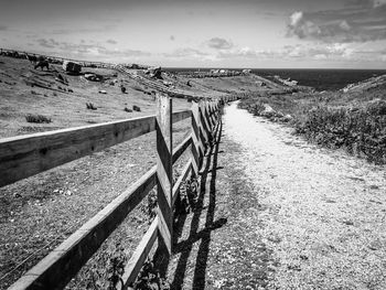 Footpath by railing on field against sky