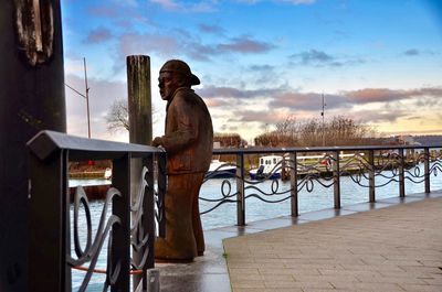 Man statue by railing in city against sky