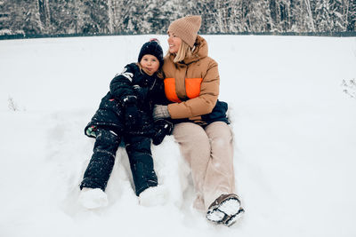 Mother and daughter sitting on snow - winter outdoors activities 