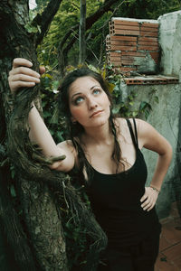 Portrait of young woman standing against tree