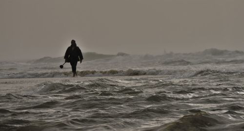 Rear view of man walking on sea shore against clear sky