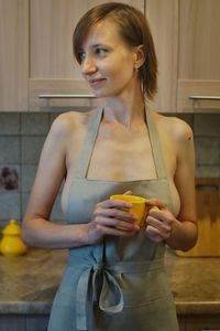 Young woman looking away while standing on table at home with the yellow cup of tea