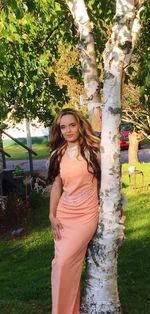 Portrait of smiling young woman standing on tree trunk