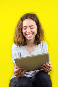 Smiling young woman using mobile phone against yellow background