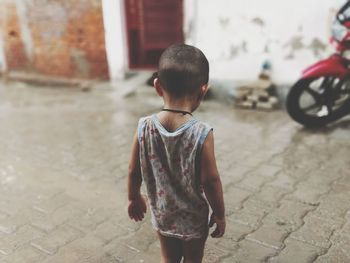 Rear view of boy standing on wet footpath