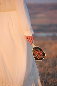 Midsection of woman holding hand mirror while standing on field during sunset