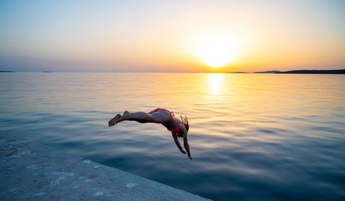 Low section of woman jumping against sea during sunset