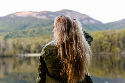 Rear view of woman standing by lake against sky