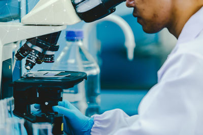 Asian male medic in uniform working with microscope making analysis at the laboratory office