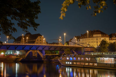 Illuminated bridge over river by buildings against sky at night