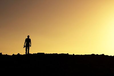 Silhouette man walking on field against clear sky during sunset